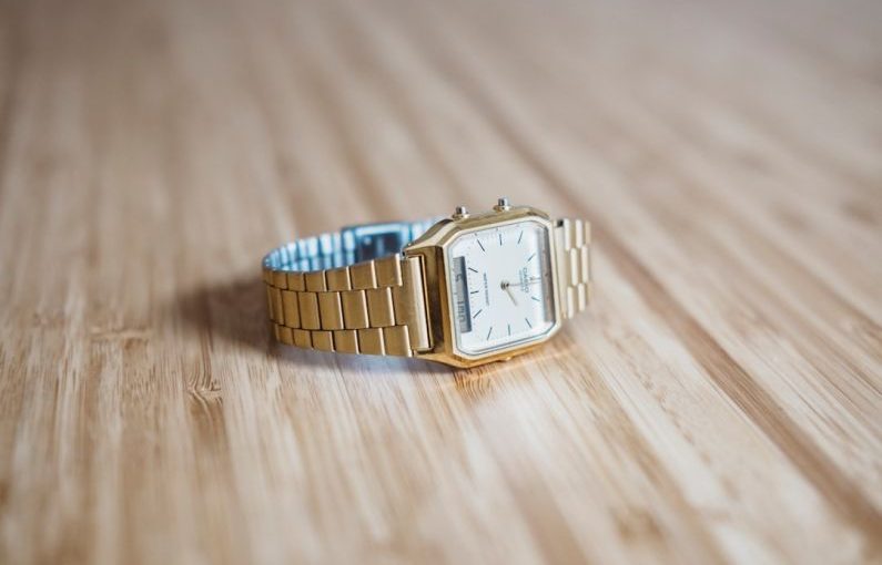 Gold Watch - square gold-colored analog watch on brown wooden board